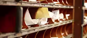 Close-up of several wooden mail slots on a wall filled with mail, envelopes, and papers. Each slot is labeled, and some have more contents than others. The image suggests a busy mailroom or office environment where the client mentioned in the case study was exposed to asbestos.