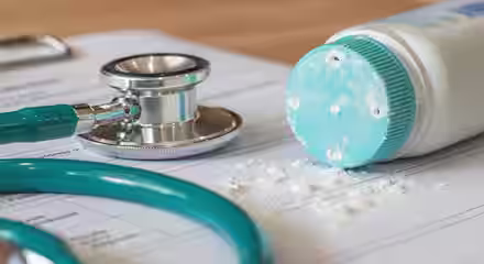 Close-up of a stethoscope and a spilled bottle of baby powder on a medical document. The baby powder is shown scattering over the paper, next to the teal-colored stethoscope, indicating a medical or healthcare setting.