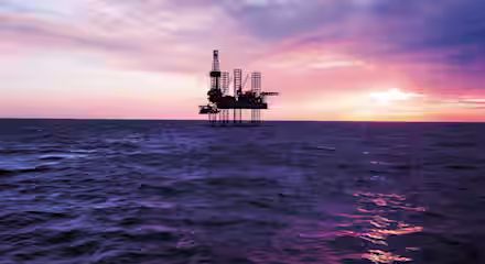 An offshore oil rig stands in the middle of a vast ocean under a dramatic sky at either sunrise or sunset. The sky is filled with a mix of purple, pink, orange, and blue hues, casting reflective colors on the water's surface.
