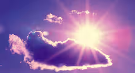 A brilliant sun shines behind a fluffy cloud in a purple and blue sky. Sun rays radiate outward, casting a warm glow around the cloud. A hint of lens flare adds an ethereal touch to the vibrant scene.