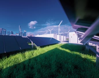 A rooftop covered with solar panels and green grass overlooks a city skyline with modern skyscrapers. Wind turbines are visible in the background under a blue sky with scattered clouds, highlighting renewable energy sources in an urban setting.