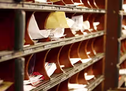 Close-up of several wooden mail slots on a wall filled with mail, envelopes, and papers. Each slot is labeled, and some have more contents than others. The image suggests a busy mailroom or office environment where the client mentioned in the case study was exposed to asbestos.