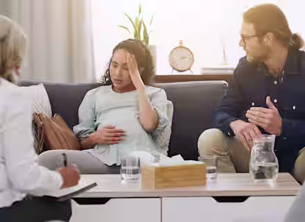 A woman sitting on a couch with a man talking to a woman.