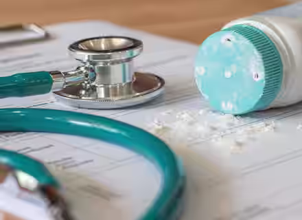 Close-up of a stethoscope and a spilled bottle of baby powder on a medical document. The baby powder is shown scattering over the paper, next to the teal-colored stethoscope, indicating a medical or healthcare setting.