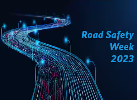 Abstract illustration of a winding road made of blue, glowing lines and surrounded by curved streetlights against a dark background. The text "Road Safety Week 2023" is written in blue on the right side of the image.
