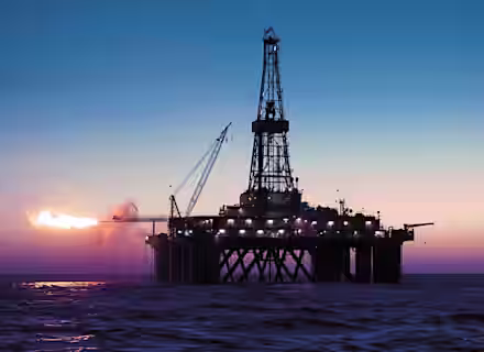 An offshore oil rig is silhouetted against a colorful sunset sky. Bright flames are seen burning from a flare stack on the left side, and various equipment and lights illuminate the platform, which is surrounded by calm ocean waters.