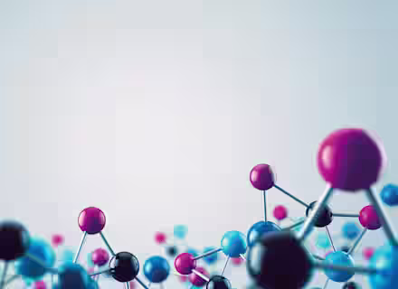 A 3D rendering of a molecular structure against a light gray background. The structure consists of interconnected spheres in various colors, including blue, black, and pink, representing atoms connected by thin rods symbolizing chemical bonds.