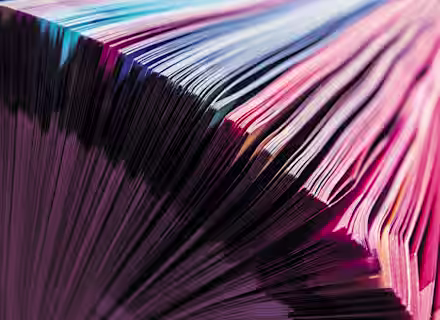 Close-up of a book with colorful pages fanned out. The edges of the pages display a spectrum of vibrant colors ranging from pink to blue, creating a striking and visually appealing pattern.