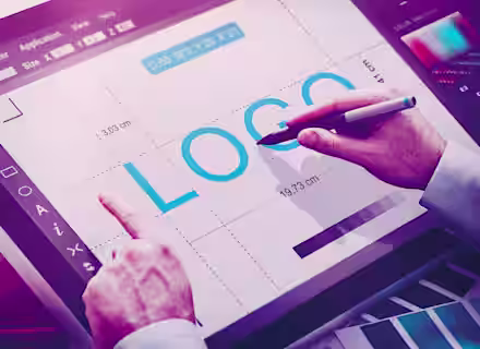 A person is working on graphic design software displayed on a digital tablet. The word 'LOGO' is prominently shown on the screen, and the person is using a stylus pen, adjusting the design elements. Various design tools and measurements are visible on the interface.