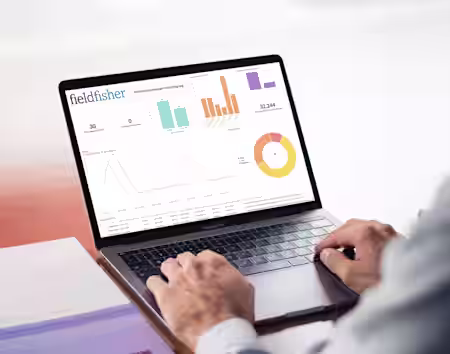 A person types on a laptop displaying various colorful graphs and charts under the heading "fieldfisher." The screen shows bar graphs, a line graph, and a pie chart, emphasizing data analysis. The person's face is not visible.
