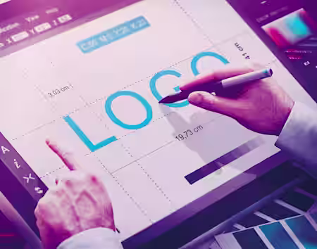 A person is working on graphic design software displayed on a digital tablet. The word 'LOGO' is prominently shown on the screen, and the person is using a stylus pen, adjusting the design elements. Various design tools and measurements are visible on the interface.