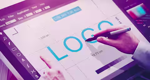 A person is working on graphic design software displayed on a digital tablet. The word 'LOGO' is prominently shown on the screen, and the person is using a stylus pen, adjusting the design elements. Various design tools and measurements are visible on the interface.