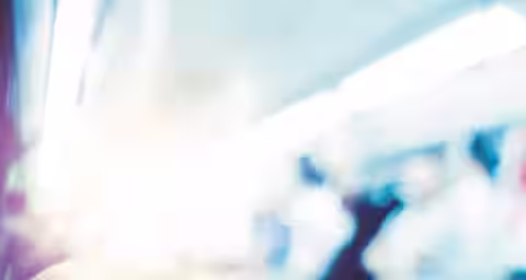 Close-up of a person's hands using a smartphone to view a graph with red and white lines and bars. The graph likely represents financial data or stock markets. The background is blurry, suggesting the person is in a busy or moving environment.