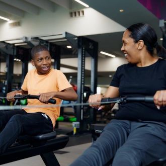 An image of a junior member and his parent, working out together on a pair of rowing machines