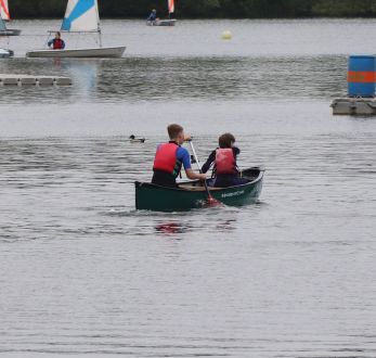 Two boys facing away paddling a green canoe on Stanborough Lake