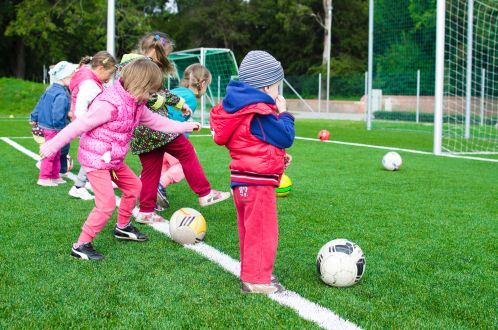 A line of children waiting in line with footballs, on an outdoor pitch