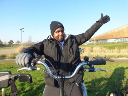 This image shows a male sitting on a push-bike with one hand in the air showing he is enjoying himself