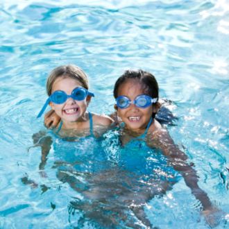 A pair of girls in a pool, grinning at the camera.