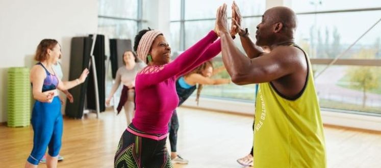 The image is of a male and a female high-fiving after completing an energetic dance class. The image is of a male and a female high-fiving after completing an energetic dance class.