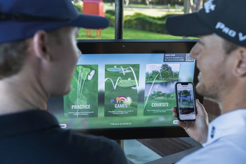 tow men on their phones next to monitors at trackman