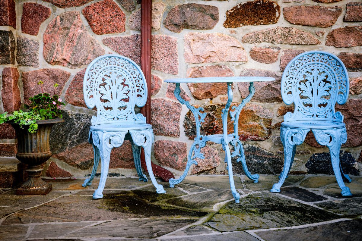 Frisch blau lackierte Metallstühle und Tisch stehen auf einer Terrasse.