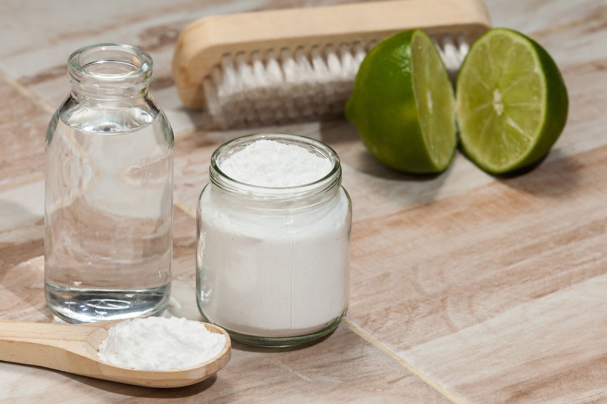 Natürliche Reinigungsmittel wie Essig und Soda bereit zur Anwendung auf Pflastersteinen, neben einer Reinigungsbürste und frischen Limetten – Symbol für umweltfreundliche Reinigungsmethoden.