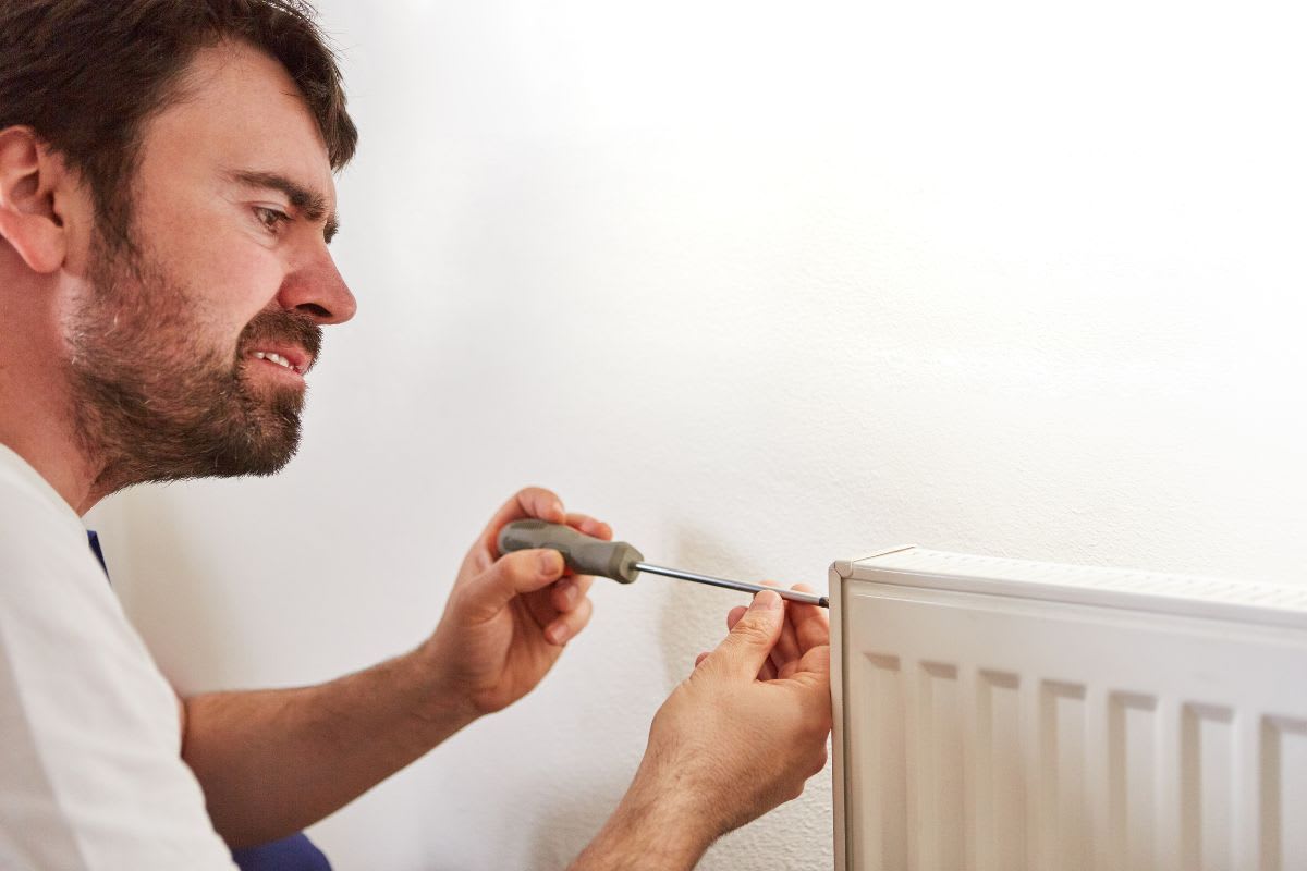 Mann beim Reparieren oder Austauschen eines Thermostats an einem Heizkörper.