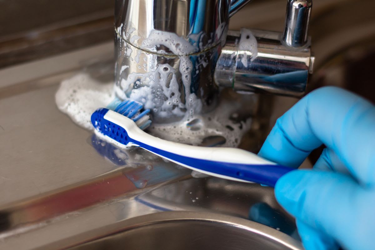 Reinigung eines verkalkten Wasserhahns mit einer Zahnbürste und Reinigungsschaum.