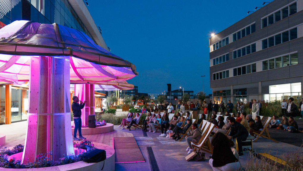 Exterior night time view of an audience watching a performance outside the People's Pavilion
