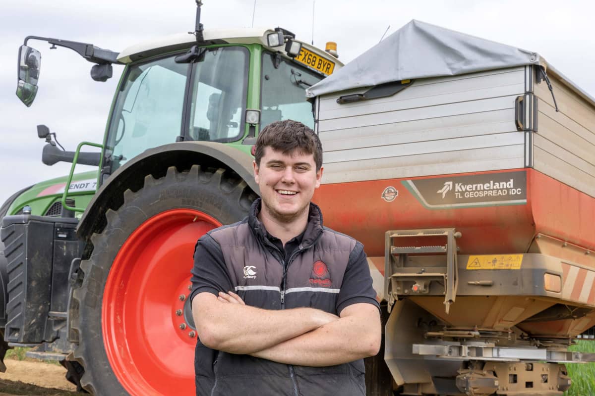 Farmer Henry Peasgood standing in front of a tractor with a Kverneland Exacta-TL GEOSPREAD iDC disc spreader, designed for precision fertilizer application in modern farming, attached to the back of it.