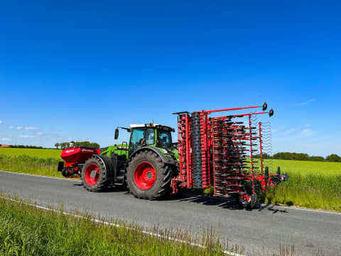 A tractor with a Kverneland u-drill seed drill on a country road beside green fields