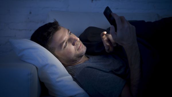 man in bed at night looking at smart device