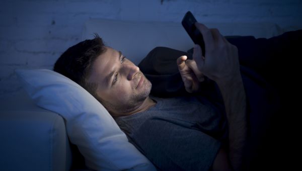 man in bed at night looking at smart device