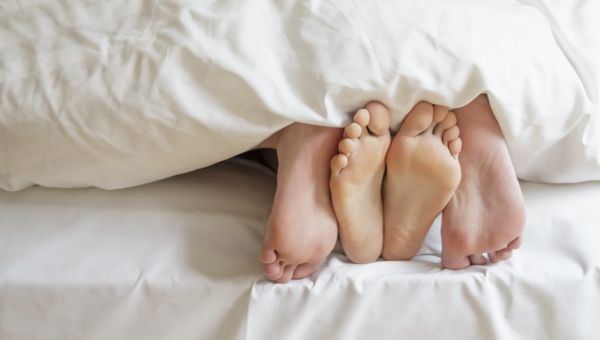 feet at the bottom of the bed, under bed sheets