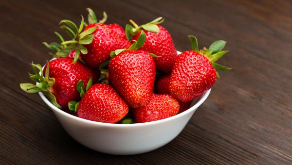 strawberries in a white bowl on a wooden tabletop