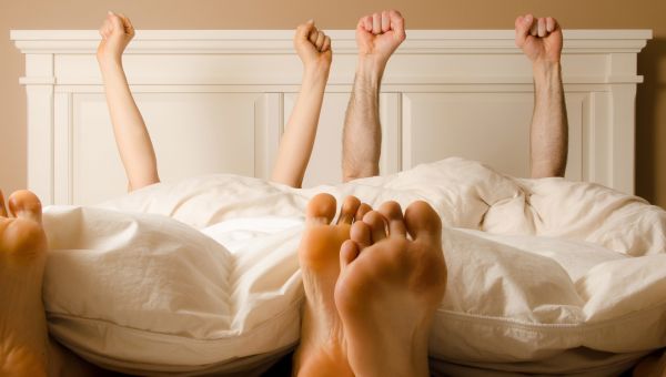 two people in bed raising their hands