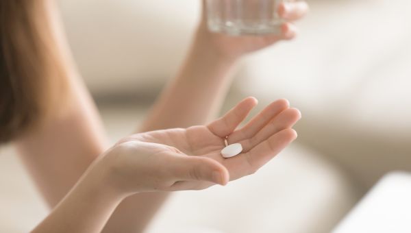 Close up shot of someone holding a pill in one hand and a glass of water in the other