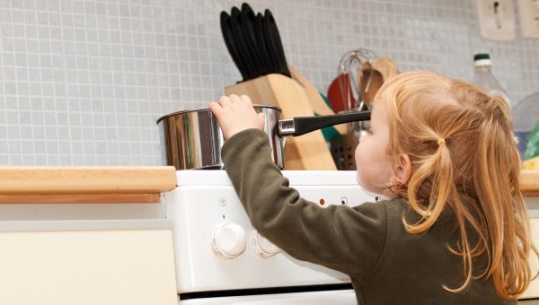 Young girl pulling pot off of stove
