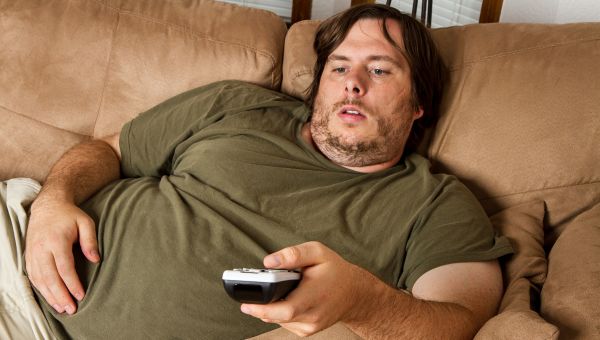 Overweight man lying on couch and watching tv
