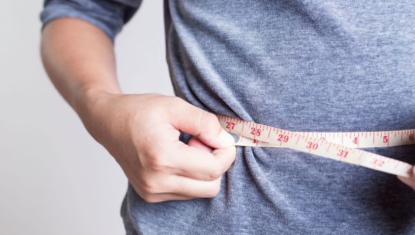 Man measures his waist side with a measuring tape.