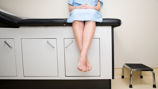 Woman sits on table in exam room.