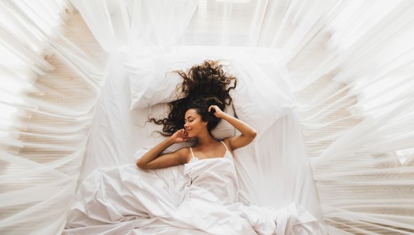 someone lies happily in bed amidst flowing sheets