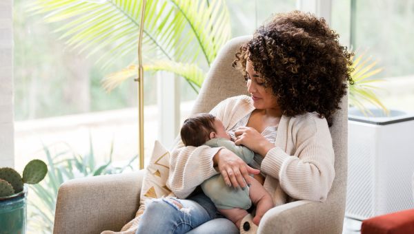 Person breastfeeding their newborn in a bright and sunny room.