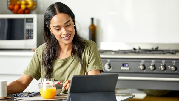 A smiling woman enjoying a bowl of yogurt and berries with a glass of orange juice for an energy-boosting breakfast.