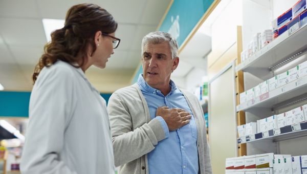 a middle aged white man speaks with a pharmacist about medicines, while placing his hand on his chest