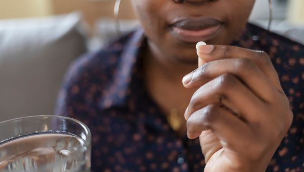 a middle aged Black woman begins to take a pill with a glass of water