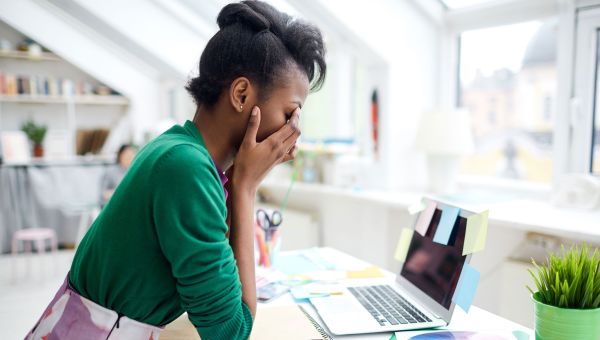 Young woman stressed at at work and holding her head in her hands at her desk