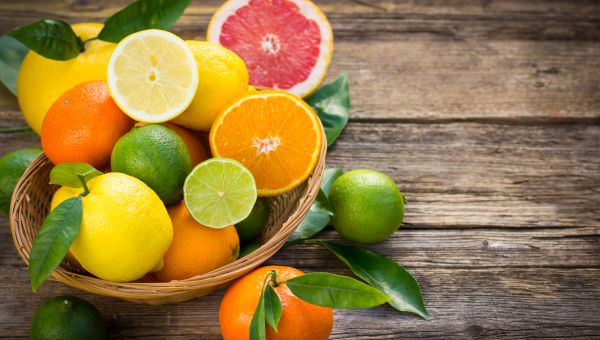 a bowl of citrus fruits including lemons, limes, and oranges, sits on a wooden table