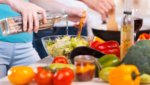 a woman pours vinegar into the salad she is preparing