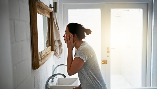 woman looking closely at face in bathroom mirror